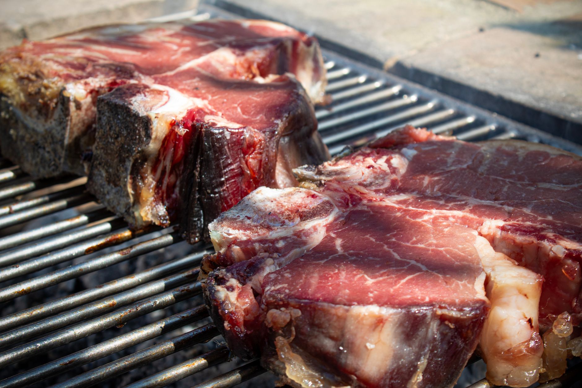 Bistecche fiorentine sfrigolano sulla griglia durante un barbecue all'aperto.