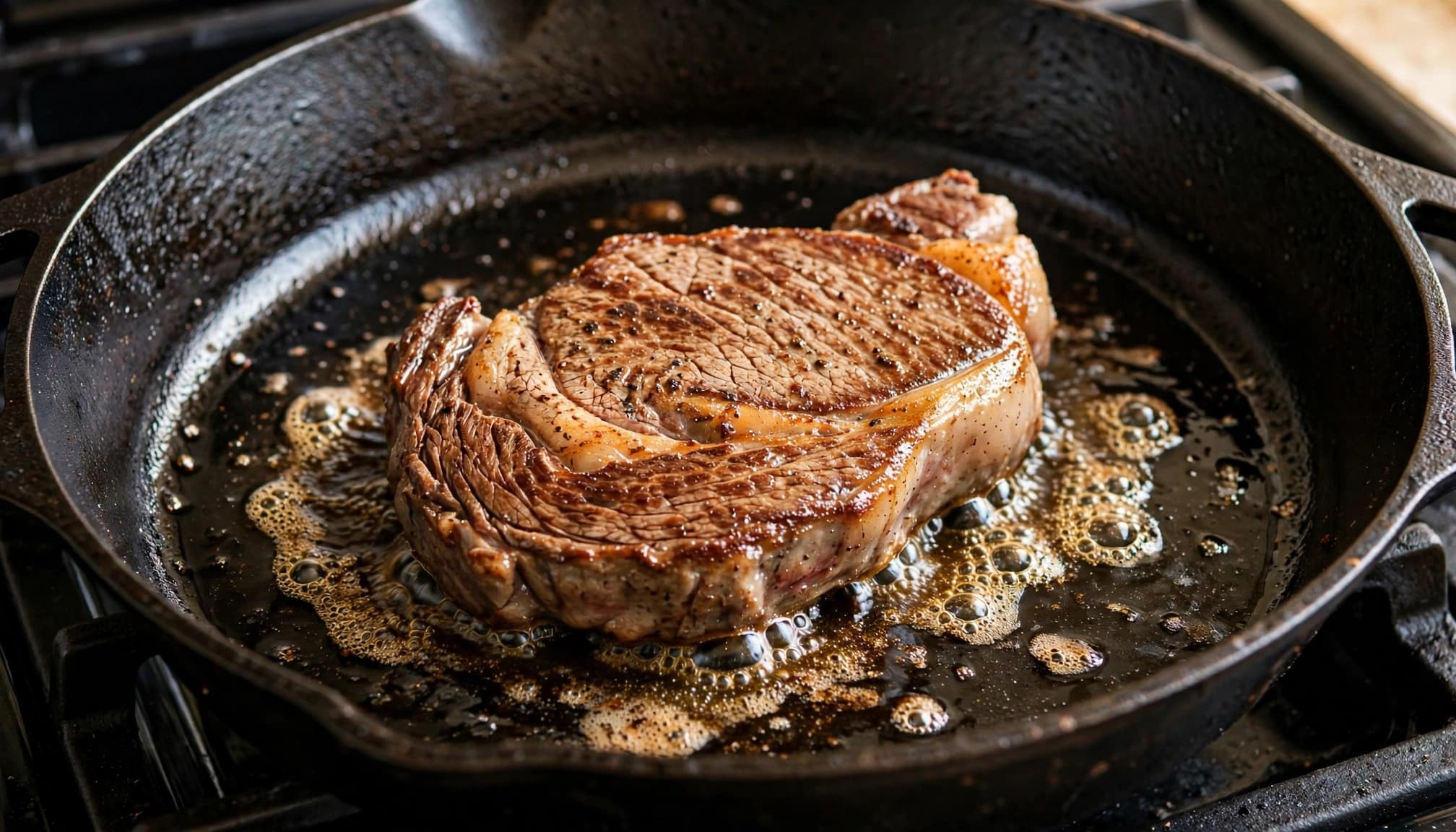 Una bistecca di manzo che cuoce in una padella di ghisa con olio sfrigolante.